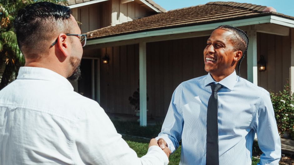Close-up of a professional handshake between a real estate agent and a client over a modern desk with a set of house keys,...